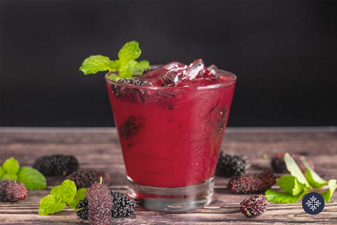 CBD cocktails: Glass with a rich, ruby red colored alcoholic drink, and mint and blackberries for garnish.