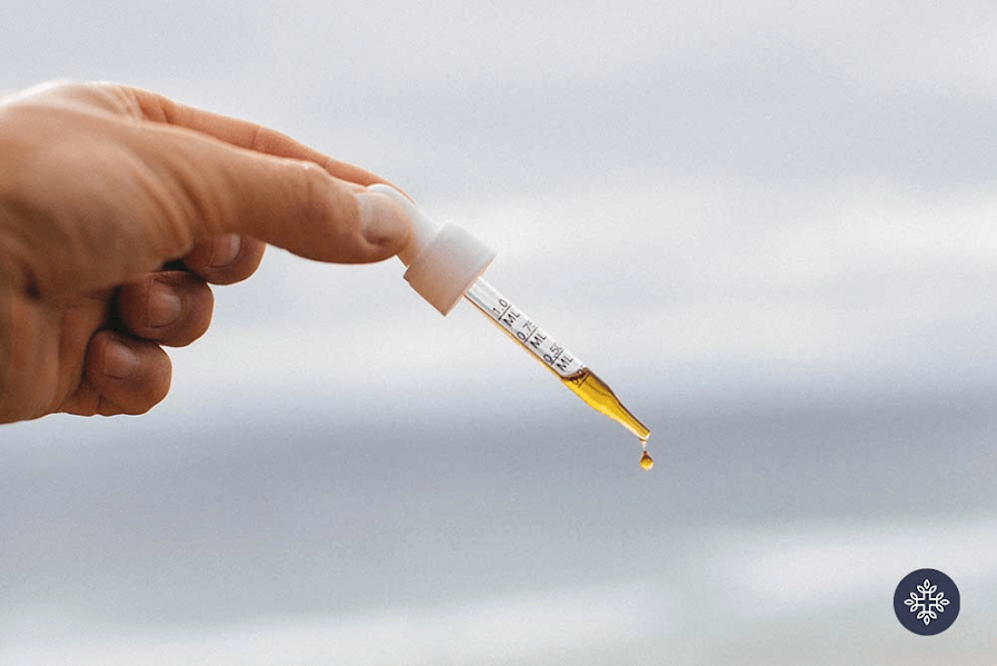 Hand holding a pipette with white handle and dropper filled with CBD oil