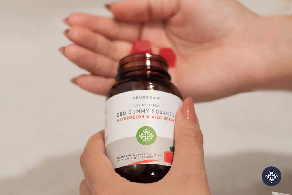 A hand holding a Neurogan CBD Gummies jar and some red gummies coming out of it