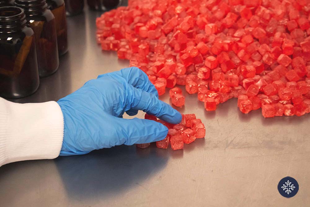 A bunch of gummies being handled by a hand with blue gloves in a lab