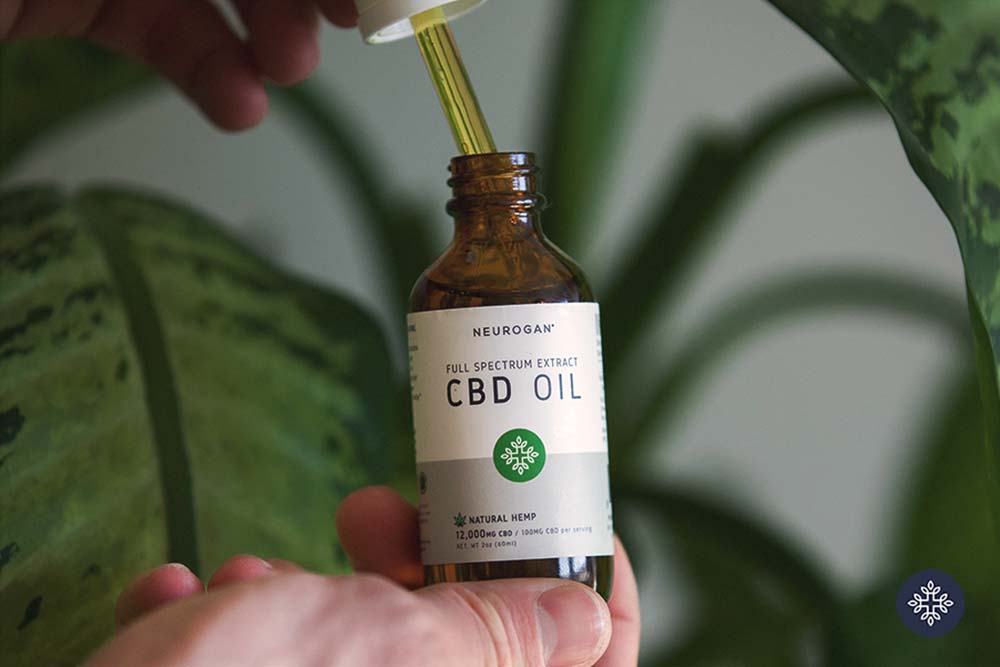 Hand holding Neurogan CBD Oil bottle and taking out the dropper full of oil