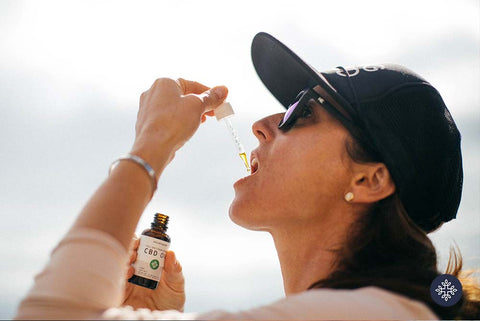 Photo of hat wearing woman administering Neurogan CBD Oil with pipette into mouth.