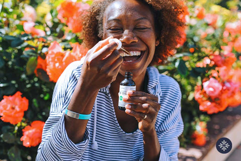 Photo of smiling woman administering Neurogan CBD Oil with pipette into mouth.