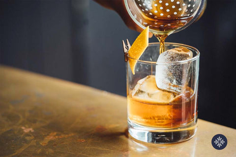 CBD Cocktails: Low ball glass with double shot of amber colored bourbon, ice cubes, and lemon garnish.