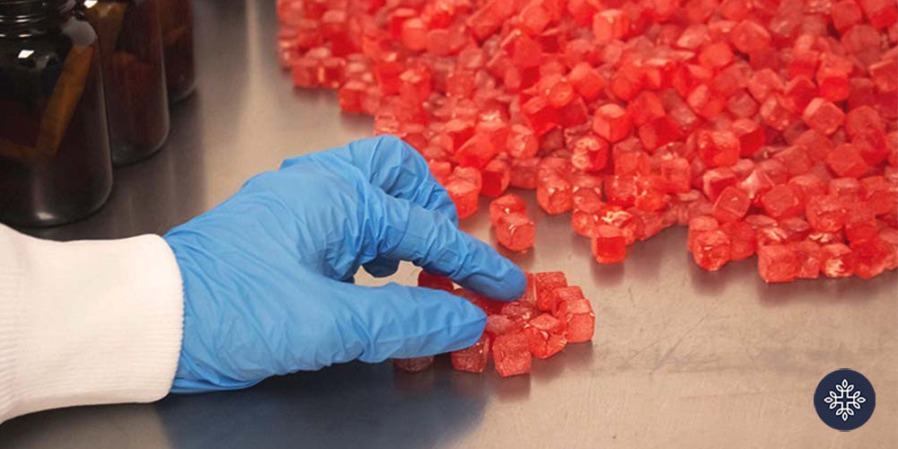 A small mountain of red CBD Gummies and a hand with a glove holding a couple of gummies