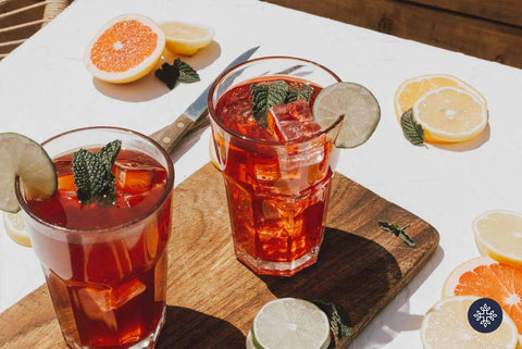 Two Glasses of Red Berry Colored CBD Cocktails With Ice and On Top of a Wooden Serving Tray