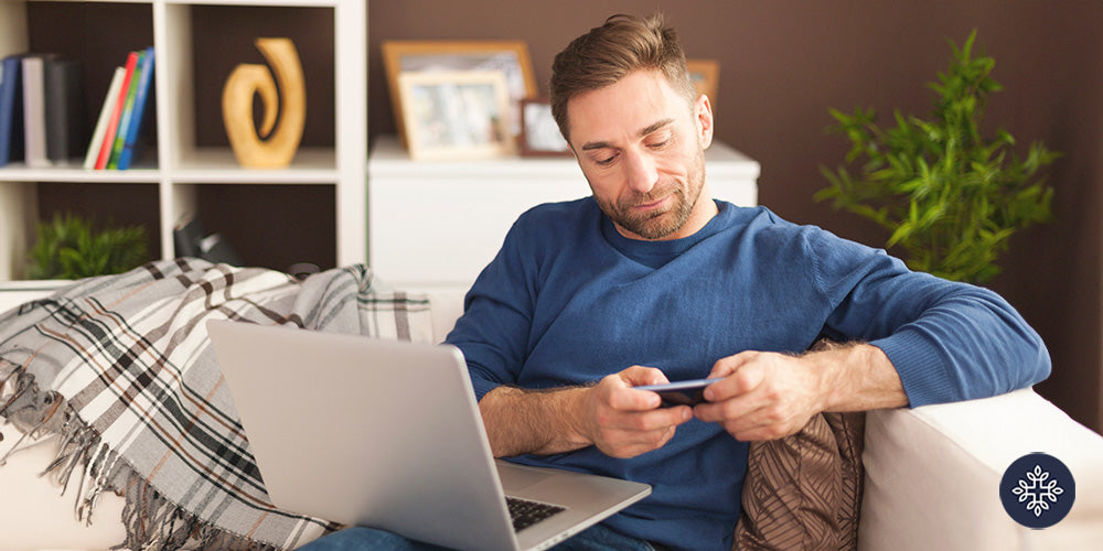 Man looking at his credit card and making a purchase on his laptop while sitting on his living room couch