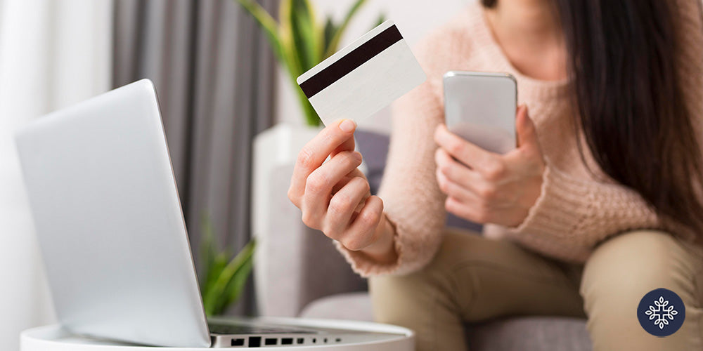 Woman holding her credit card and phone while looking at a laptop