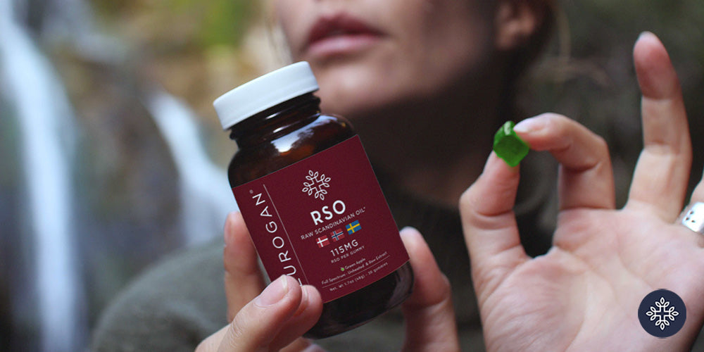 A woman holding a jar of Neurogan RSO Gummies and a green gummy in front of a cascade