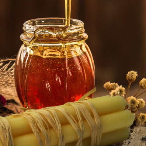 beeswax dinner candles in front of a glass pot of honey and dried flowers