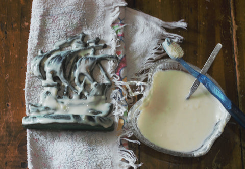 vintage brass ship covered in white paste sitting on a tea towel next to a glass apple shaped bowl filled with white paste and a teaspoon on a wooden coffee table