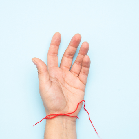 fair skinned hand with, open palm with palm faced upwards. Red string tied around the wrist. Hand laying on a blue background