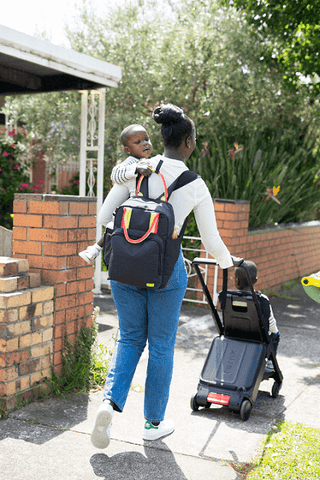 Mother pushing suitcase stroller with one hand and carrying child on the other