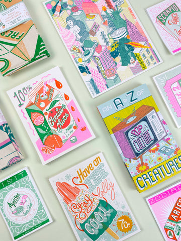 Jacqueline's illustrated products including tea towels, art prints and a book are laid out on a mint background