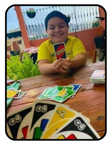 Boy smiling playing UNO with one card left, opponent has 3 +4 cards & a +2 card