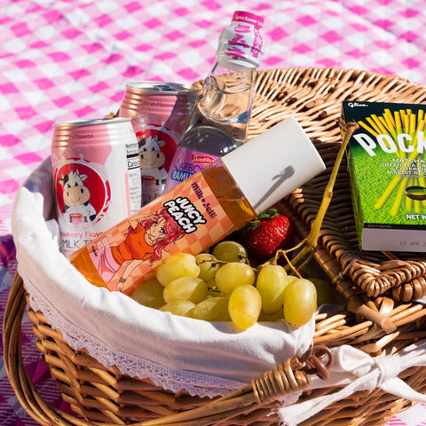Milk Jelli's Juicy Peach body mist sits in a picnic basket surrounded by fruit and sweets.