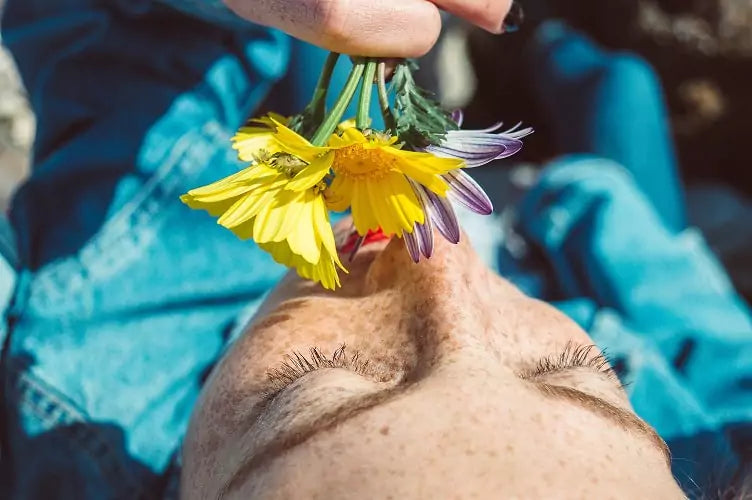 Roodharige vrouw met sproeten die ligt en aan een bloem ruikt