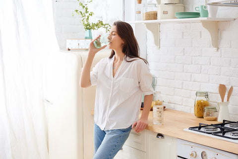 A woman drinking water from a glass in a kitchen, promoting optimal health and balanced diet