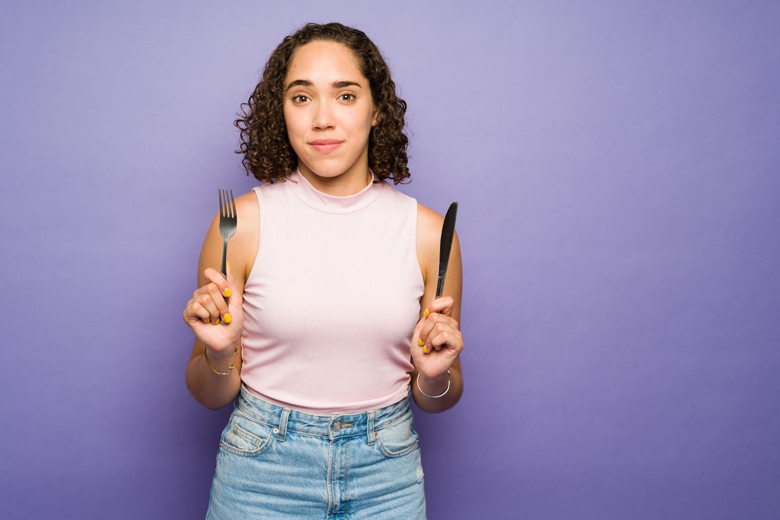 Young woman with fork and knife on purple background, symbolizing healthy meal choices and managing cravings