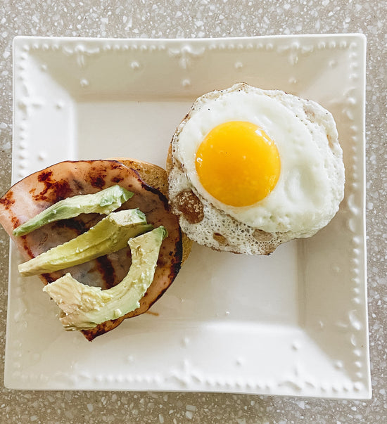 sandwich with Canadian bacon, egg, and avocado on top of a white plate