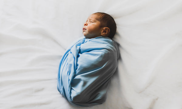 Swaddled infant asleep on a white sheet