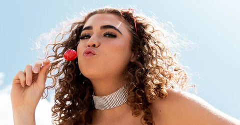 Home lash extension kit showcased on a confident woman with curly hair holding a red lollipop
