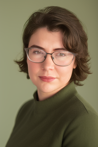 Portrait of a woman with short hair wearing cat-eye glasses and a green turtleneck, giving a gentle smile against a soft green background.