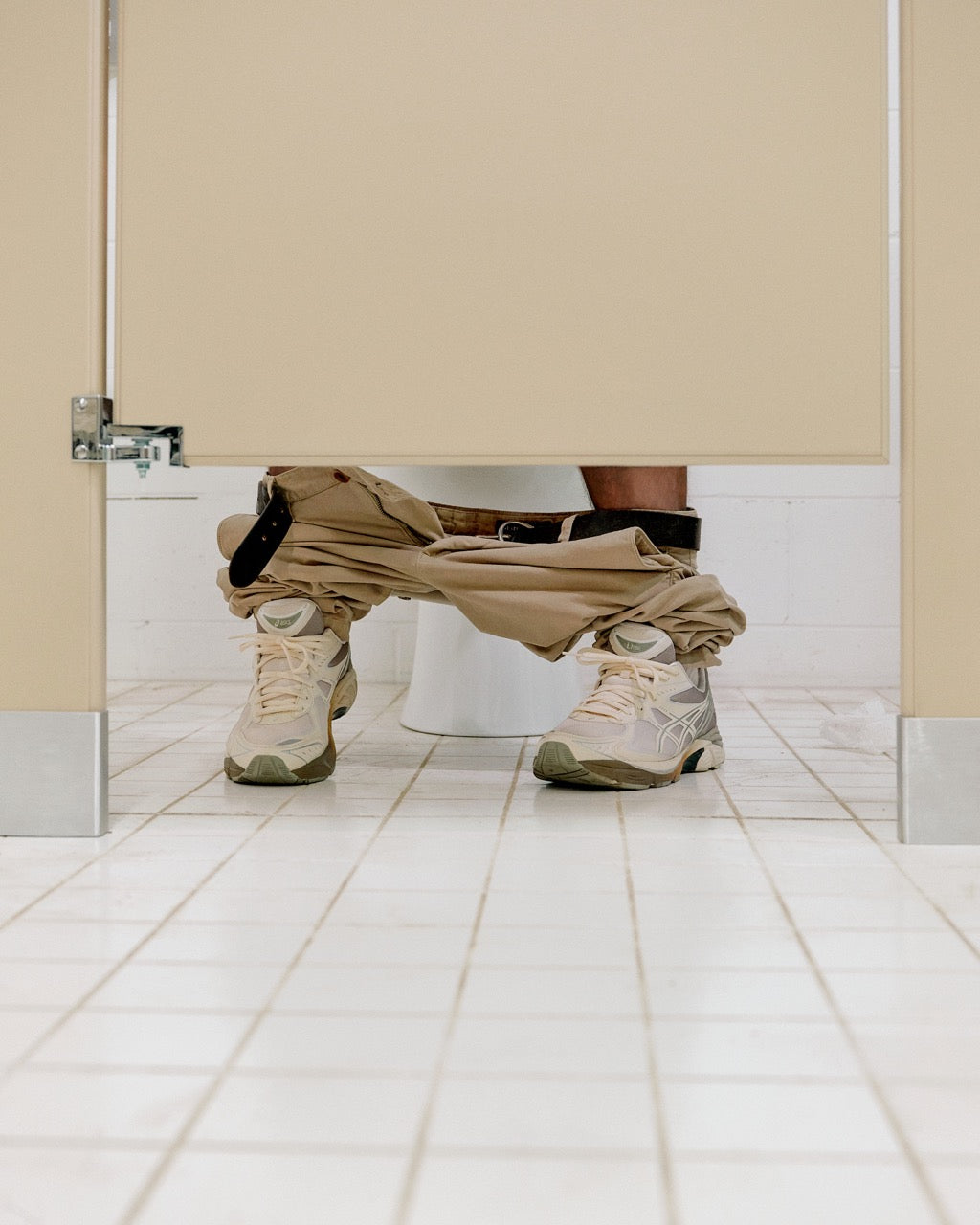 Unique perspective photo featuring a person sitting in a bathroom stall, pants lowered to ankles, with Dime x ASICS GT-2160 sneakers prominently displayed, underscoring their everyday usability and distinct style.