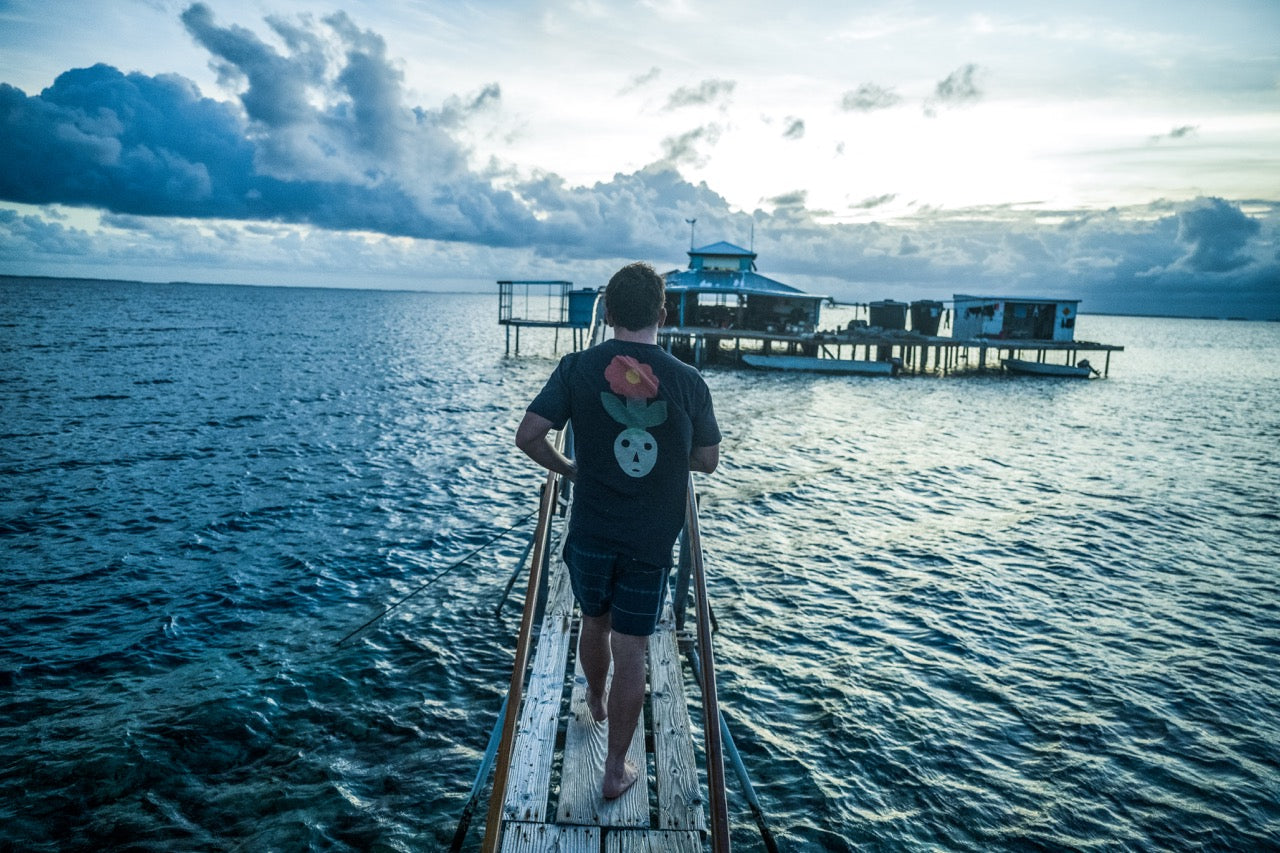Man on an adventure in Tahiti wearing the Roark Deep Roots Premium Tee in Black walking down a dock over the water