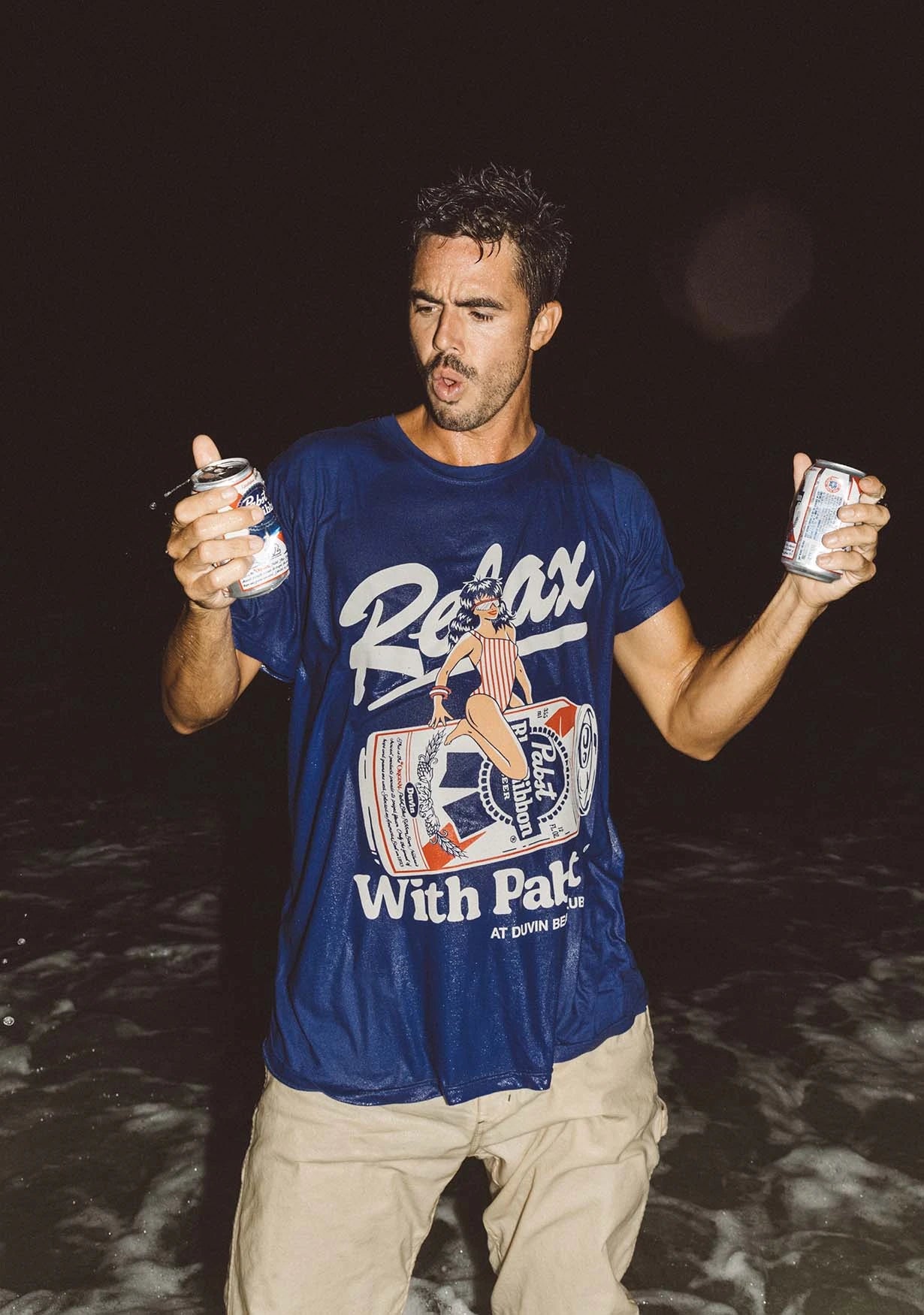 Image of a guy standing the ocean wearing the Duvin x PBR Wave Rider Tee in Blue