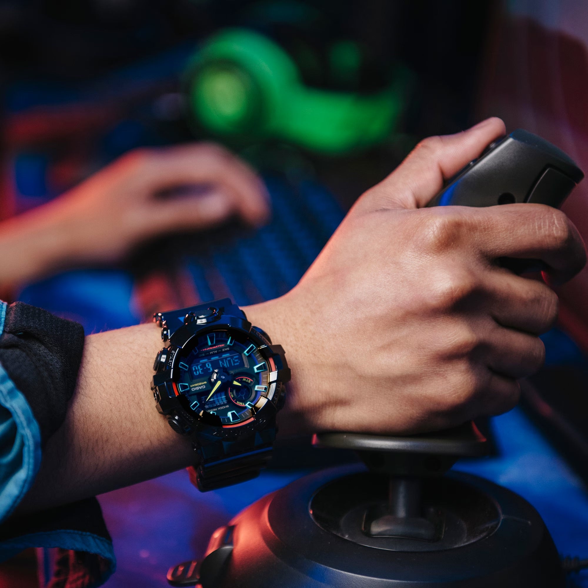 Person immersed in playing video games, wearing the G-SHOCK GA-700RGB-1A with vibrant color accents, enhancing their gaming setup.