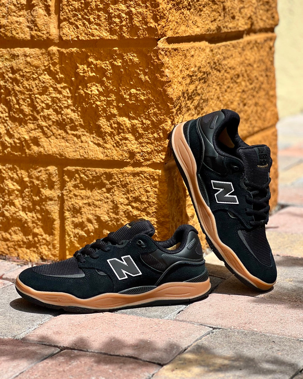 Image of the New Balance Numeric Tiago Lemos 1010 Skate Shoes in Black Gum sitting up next to a brick wall. 