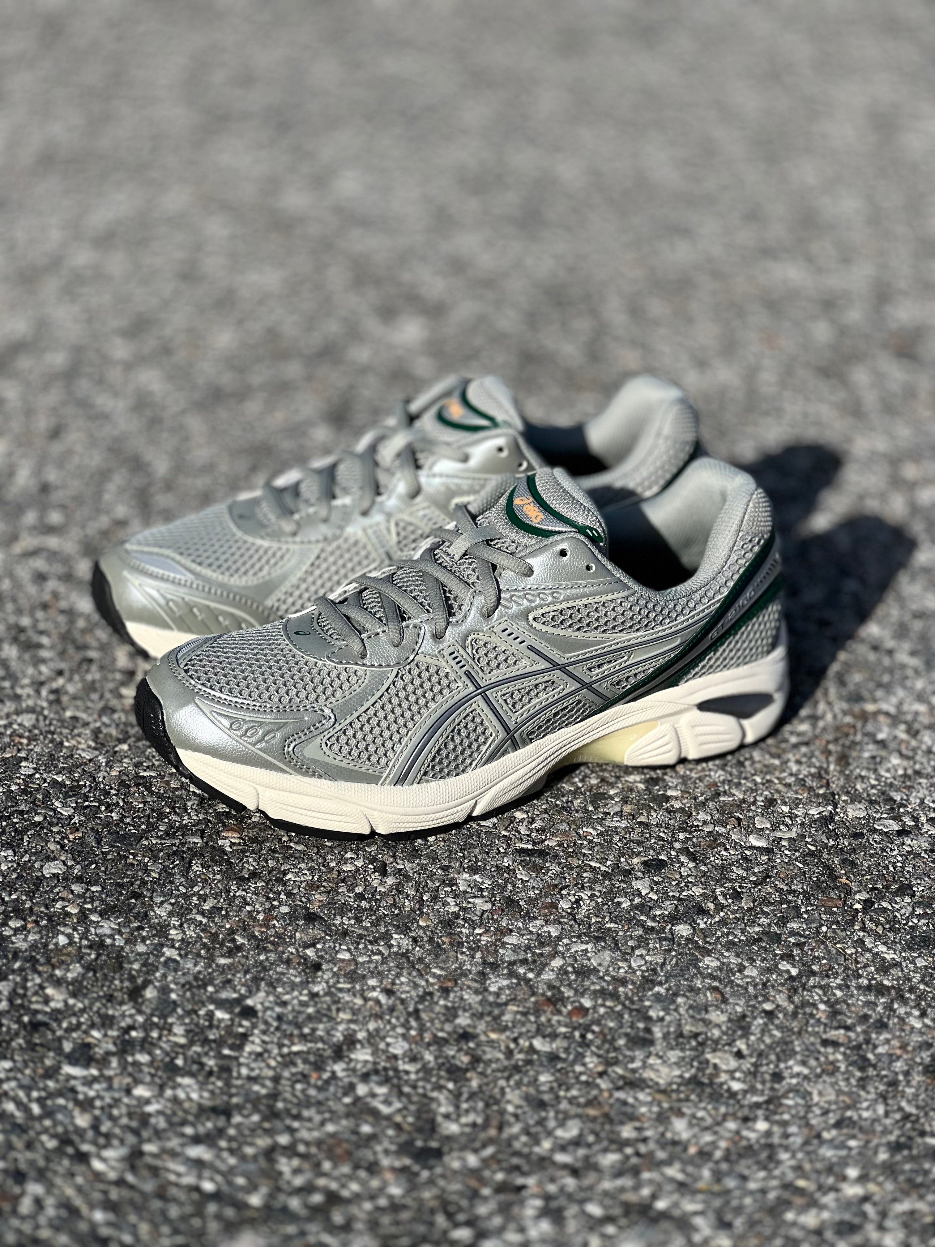 ASICS GT-2160 in Seal Grey/Jewel Green showcased on the concrete at Drift House Cocoa Beach parking lot.