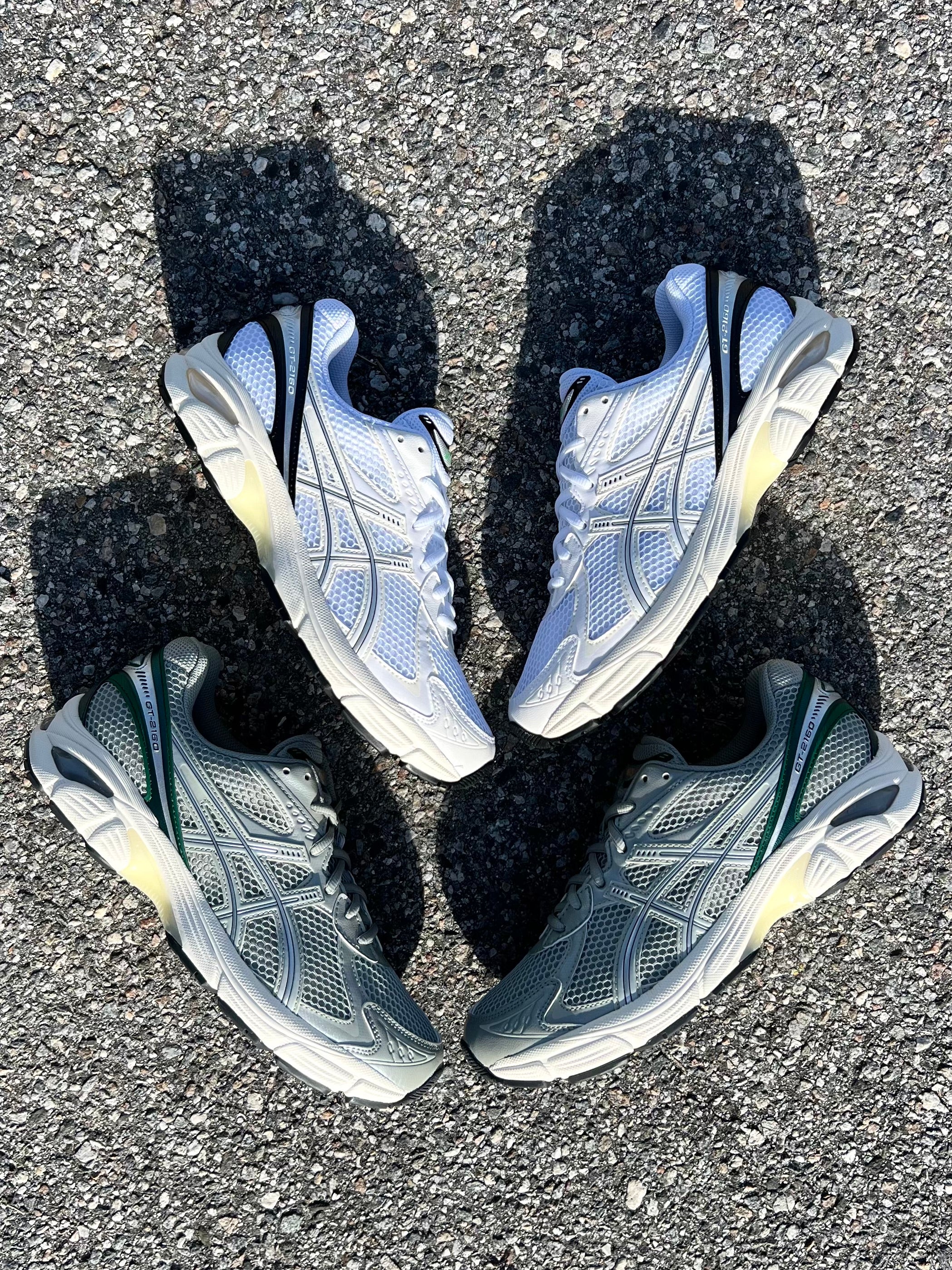 ASICS GT-2160 Seal Grey/Jewel Green and White/Black sneakers displayed on concrete at Drift House Cocoa Beach parking lot.