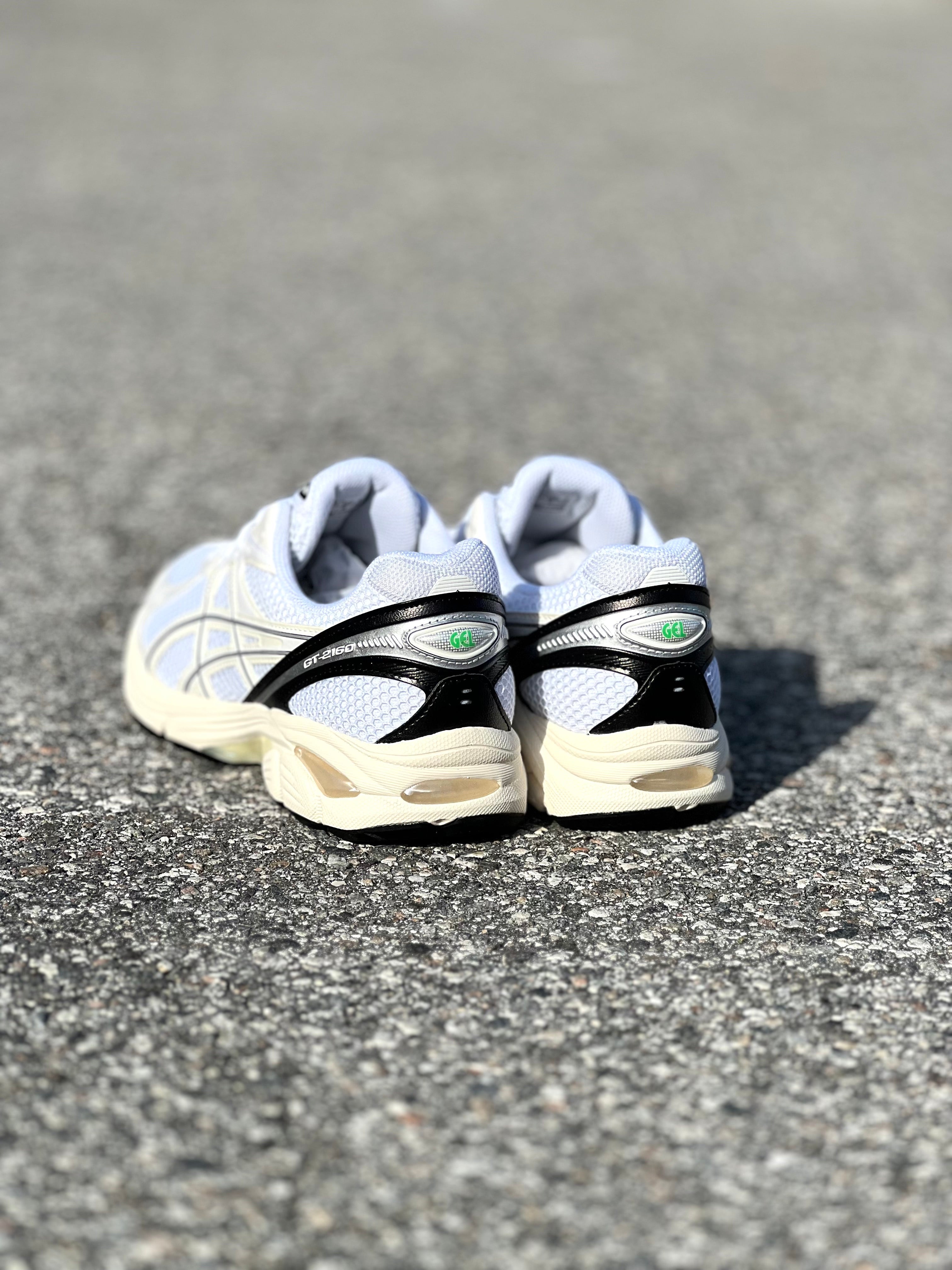 ASICS GT-2160 in White/Black with off-white oxidized sole, featured on the concrete at Drift House Cocoa Beach parking lot.