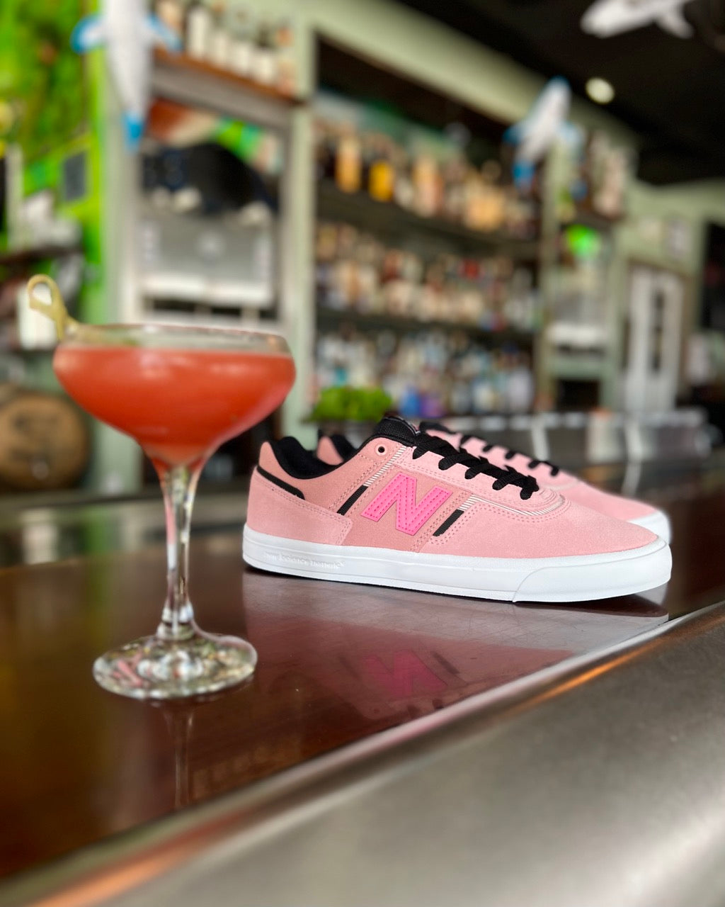 Image of the New Balance Numeric Jamie Foy 306 Flamingo Pink Skate shoes sitting utop a bar next to a fruity drink