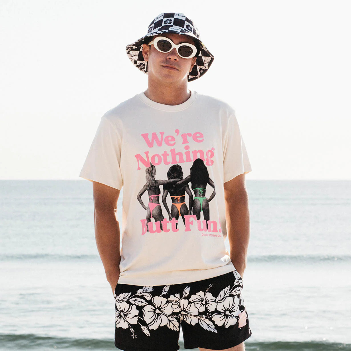 Man on beach, wearing Duvin's Fun Tee, sandy shore and ocean waves in the background.