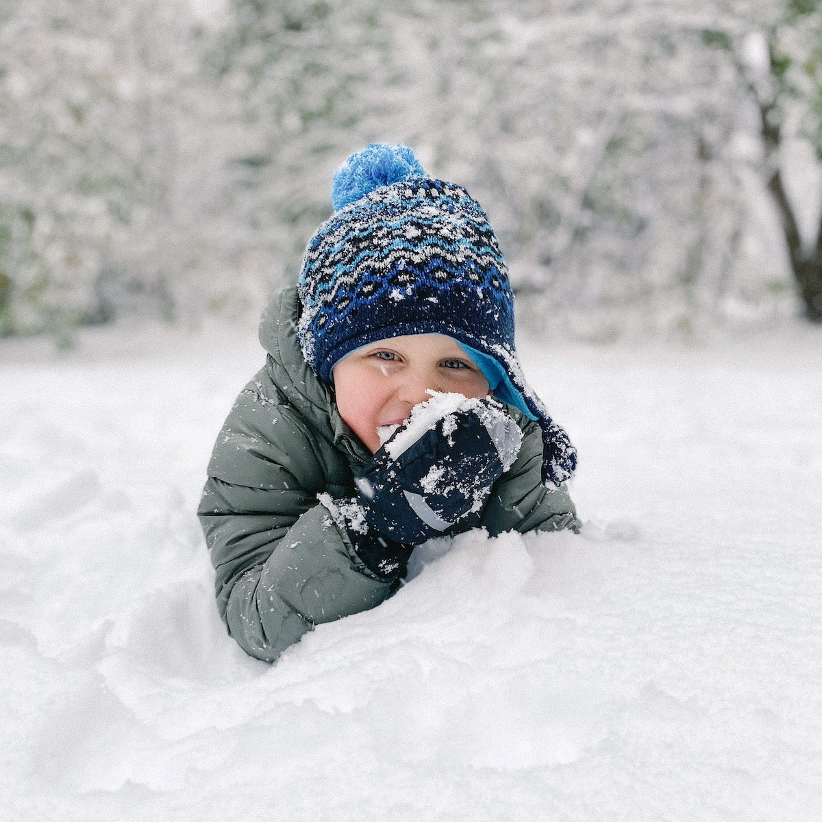 a boy sitting in a pile of snow eating snow.