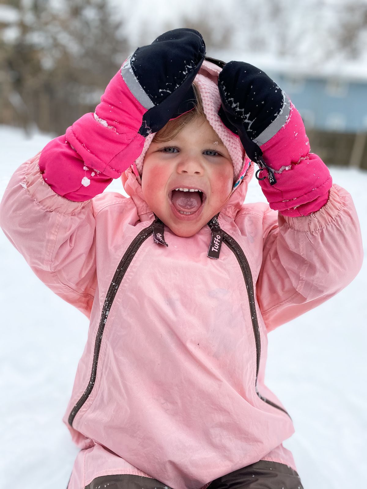 little girl in pink snowsuit and mittens playing in the snow.