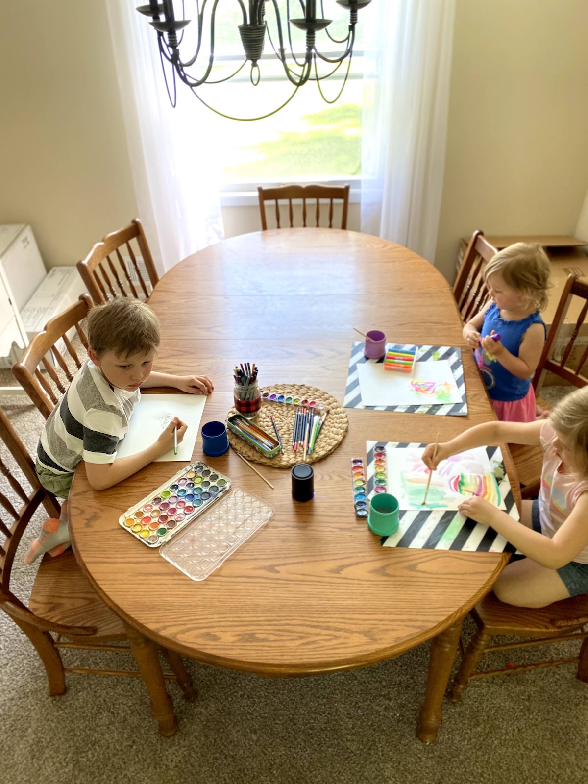 three kids watercoloring at a big table.
