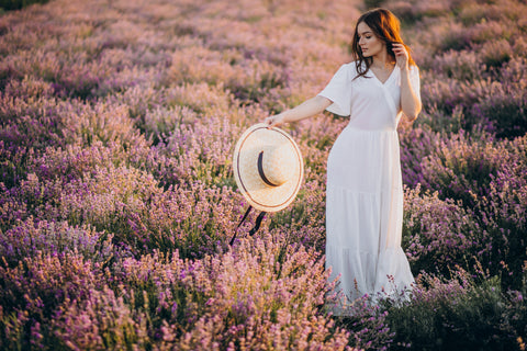 Woman in white dress holding a hat walking on a flower field