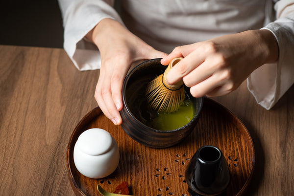 Matcha Zubereitung (Hand hält Besen in der Hand und verrührt das Matcha Pulver)