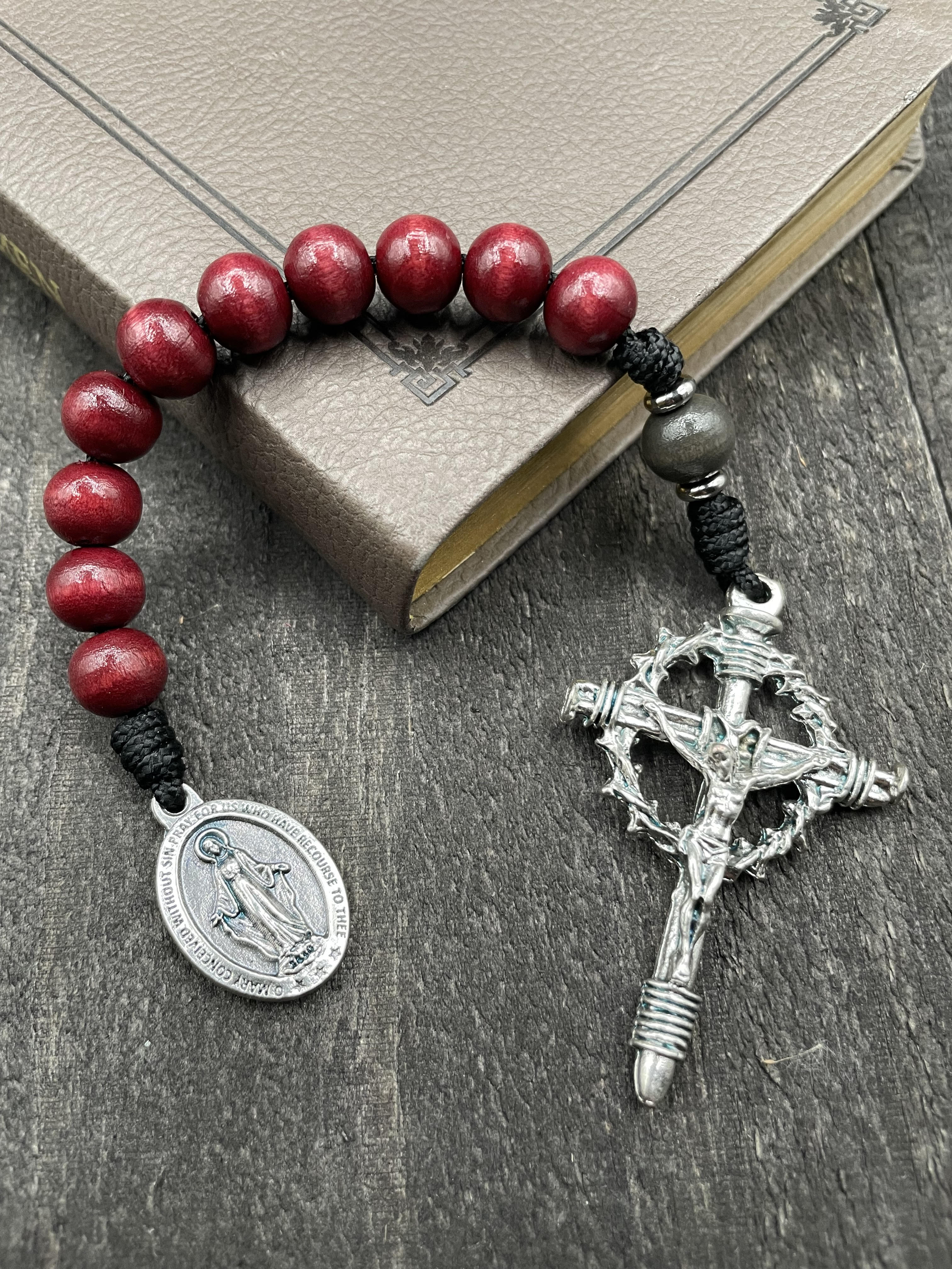Close-up of a rosary with vibrant red beads, red knot accents, and a detailed silver crucifix featuring a thorny crown and a silver pendant of Mary, displayed on a book on a light surface, ideal for prayer and devotion.