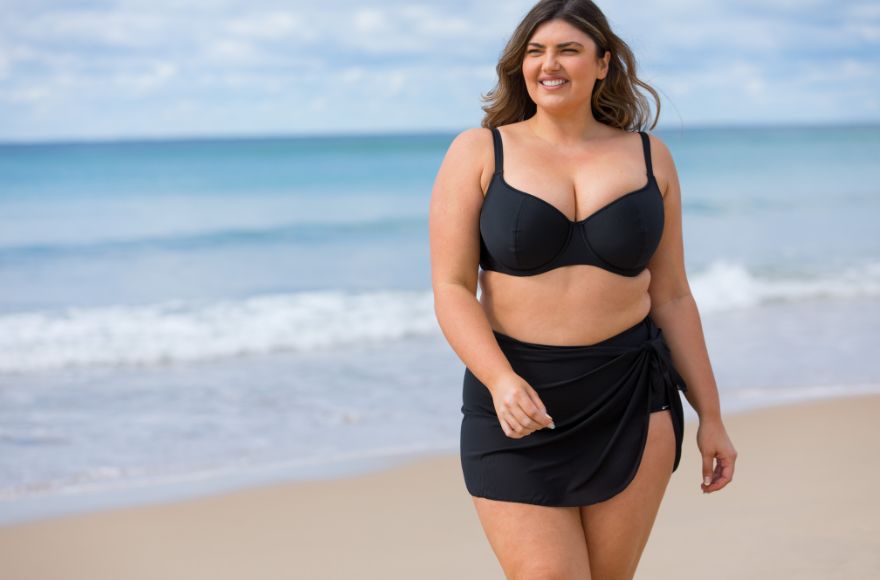 Woman with long brown hair wears black bikini with short mesh skirt at the beach