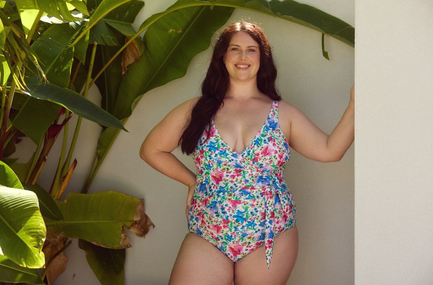 Woman with long brown hair wears bright floral one piece swimsuit