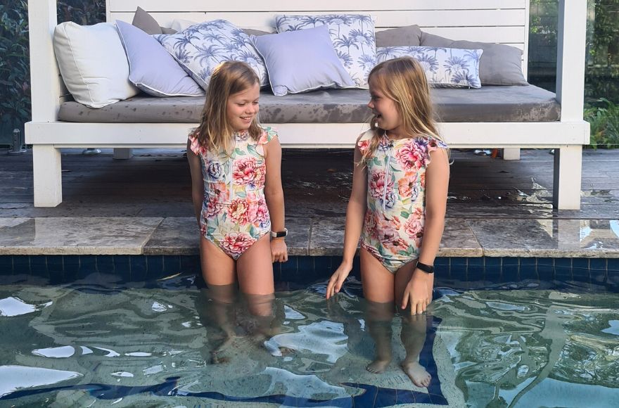 Two girls pose in the pool wearing matching Positano White frill sleeve zip up one piece swimsuits