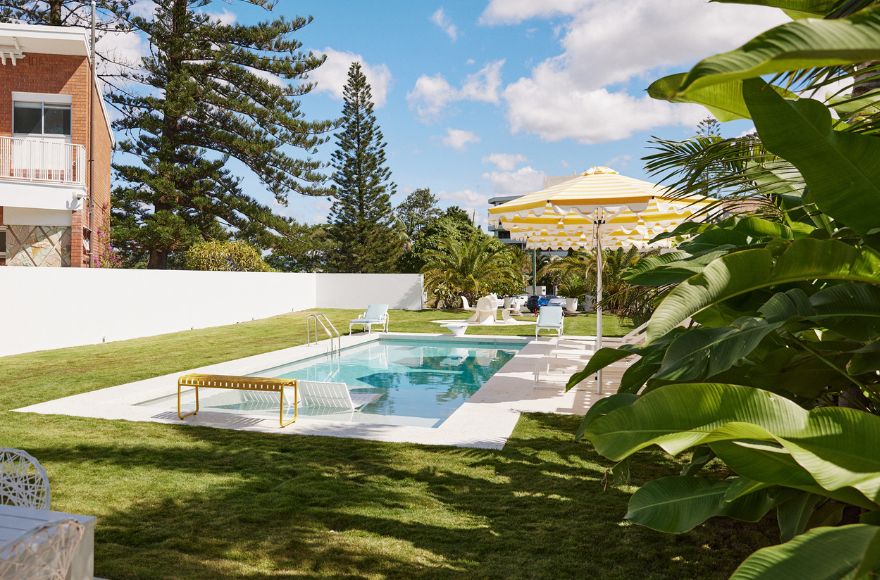 A Slim Aarons inspired pool is surrounded by green lawn and tropical gardens.