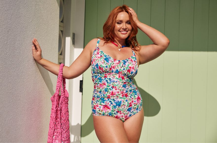 Woman with red hair wears a bright floral swimsuit with a colourful beaded necklace