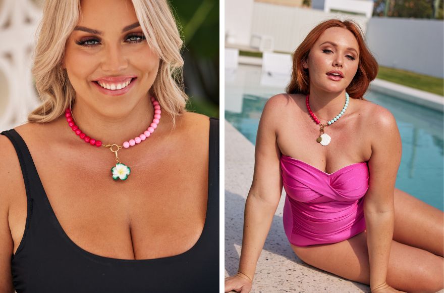 Woman with blonde hair wears black swimsuit with pink beaded necklace. Woman with red hair poses by the pool wearing a bright pink swimsuit with a pink and light blue beaded necklace.