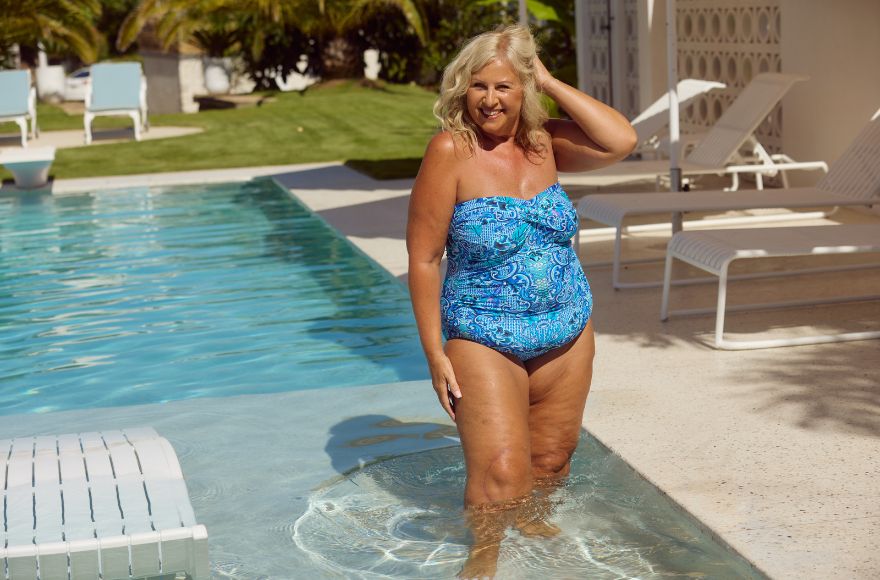 Woman with blonde hair stands in the pool wearing a strapless blue swimsuit